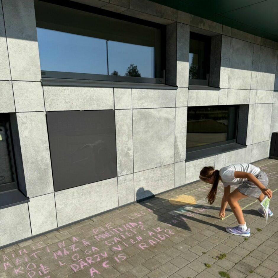 meitene ar krītu raksta uz asfalta