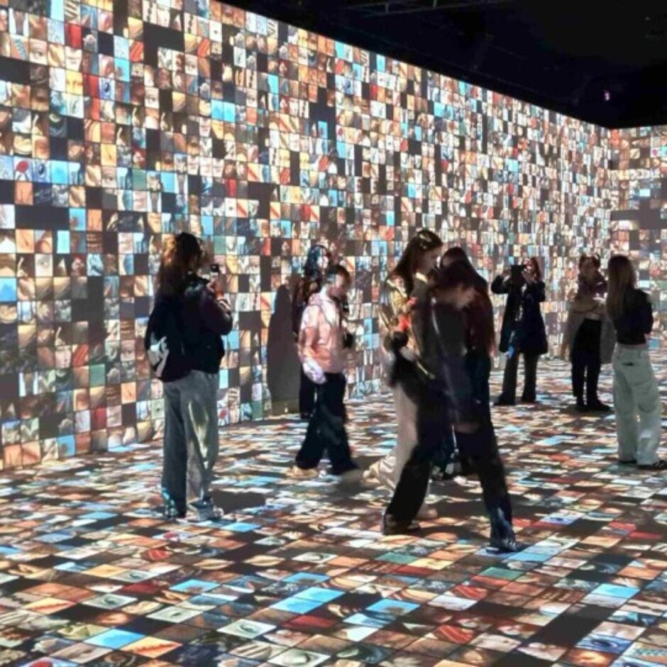 Liela telpa ar sienām un grīdu, ko klāj neskaitāmu mazu fotogrāfiju projekcijas. Dažāda vecuma cilvēki, tostarp bērni, vēro attēlus un fotografē ar tālruņiem, baudot ieskaujošu digitālās mākslas izstādi.