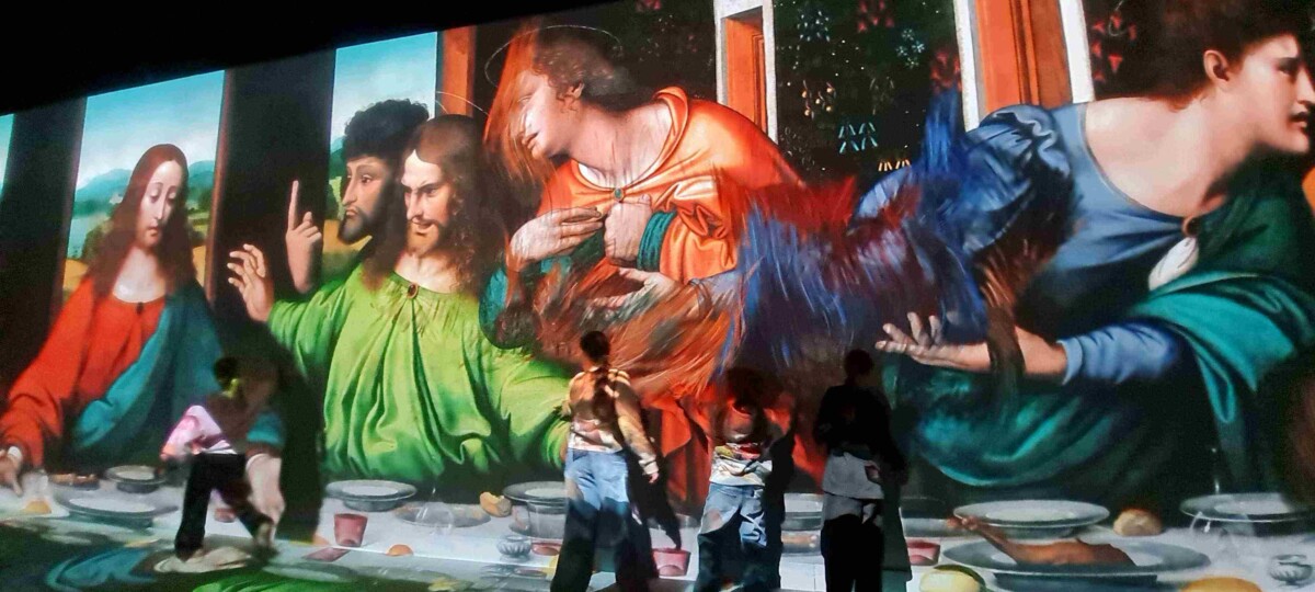 Ieskaujoša projekcija attēlo lielformāta gleznu ar Bībeles ainu, piemēram, Pēdējās vakariņas, uz sienas un grīdas. Redzami daudzi tēli pie galda, un vairāki cilvēki stāv priekšā projekcijai, vērojot to.
