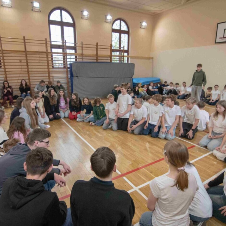 Skolēni veic grupu darbu sēžot aplī sporta zālē