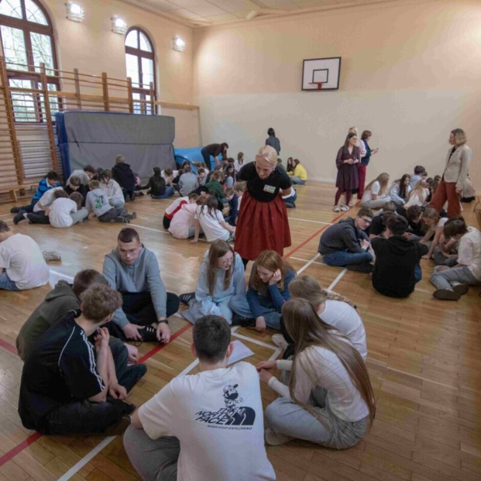 Skolēni veic grupu darbu sēžot aplī sporta zālē