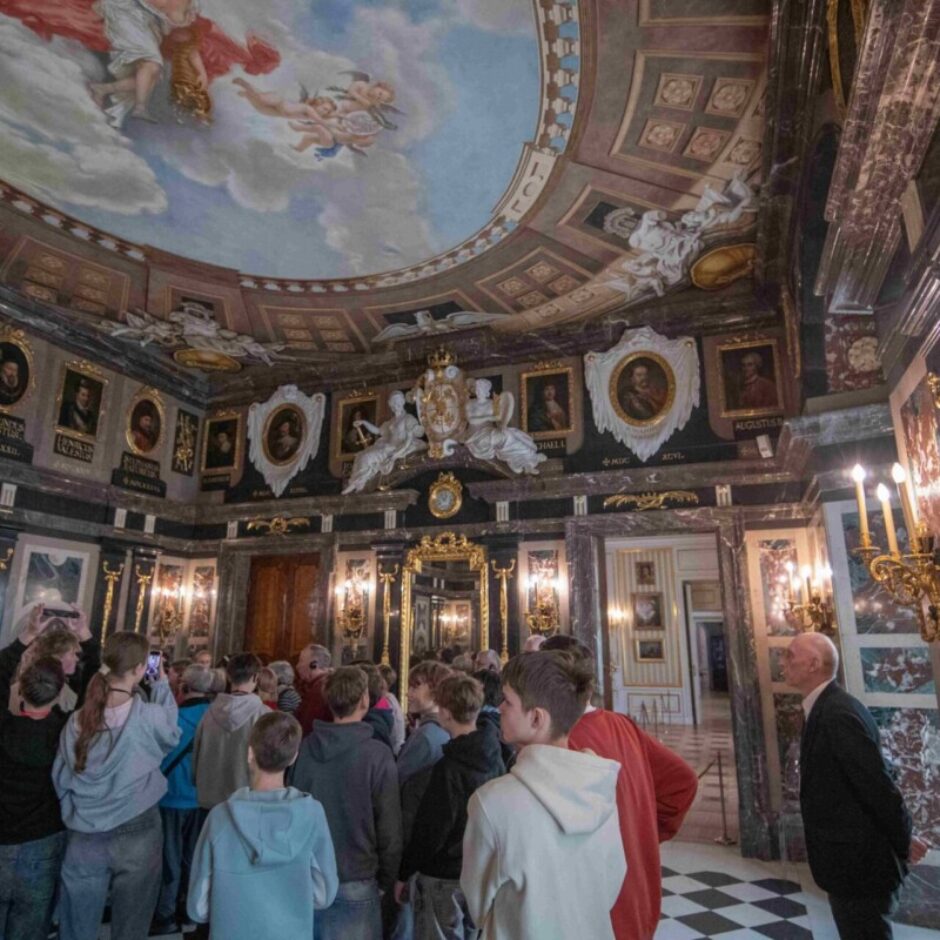 Greznā zālē ar apgleznotiem griestiem, kas attēlo debesis ar eņģeļiem un puttiem. Sienas klāj tumši marmora paneļi, un tās rotā neskaitāmi portreti zeltītos rāmjos, baltas skulptūras un zeltīti sienas svečturi. Redzami uzraksti 