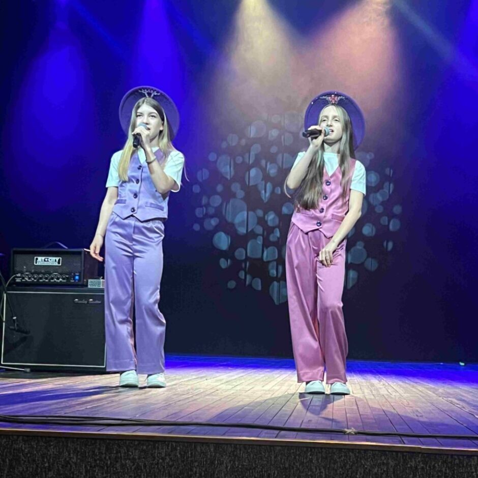 Divas jaunas smeitenes dzied uz skatuves, viena violetā, otra rozā, tērpušās pieskaņotos vestēs, platmalu cepurēs un platās biksēs. Abas tur mikrofonus, un viņas apgaismo skatuves prožektori uz tumši zila fona ar gaismas rakstu. Skatuves kreisajā pusē redzams pastiprinātājs ar uzrakstu 