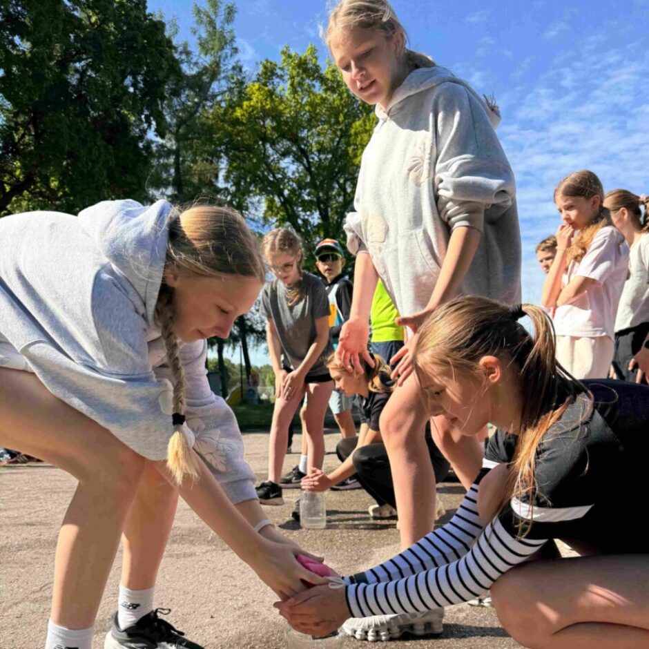 skolēni pilda stafetes uzdevumu - piepilda burku ar ūdeni