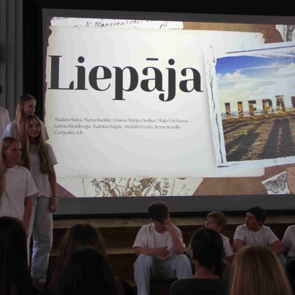 Pusaudži telpā ar lielu projektora ekrānu, uz kura redzams uzraksts 