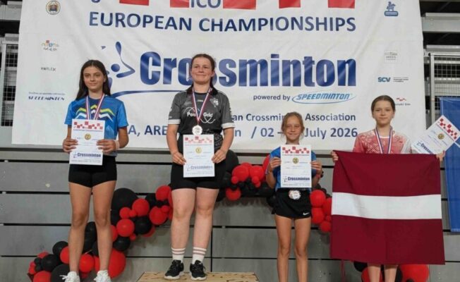 Četras jaunas meitenes stāv uz pjedestāla ar medaļām un diplomiem pēc 