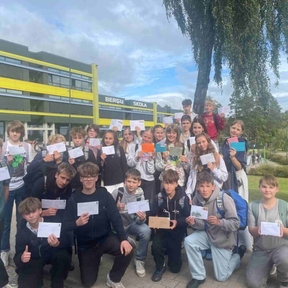 Pusaudžu grupa stāv ārā, pie skolas ēkas ar uzrakstu 