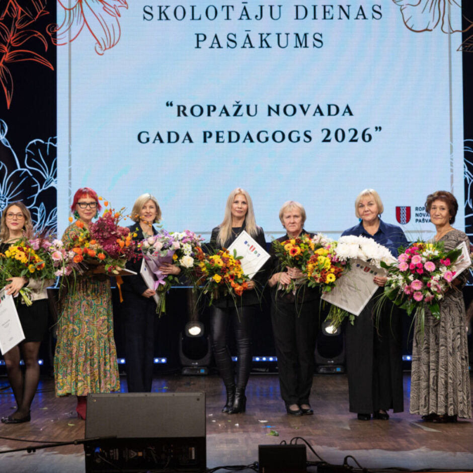 Deviņas sievietes stāv uz skatuves, turot krāšņus ziedu pušķus un sertifikātus. Aiz viņām redzams liels ekrāns ar uzrakstiem 