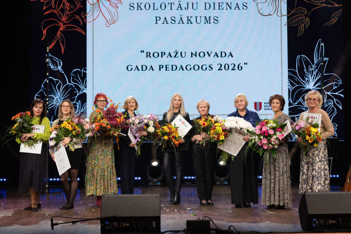 Deviņas sievietes stāv uz skatuves, turot krāšņus ziedu pušķus un sertifikātus. Aiz viņām redzams liels ekrāns ar uzrakstiem 